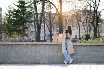 Woman with a shopping bags chatting by phone in a city park after shopping time   