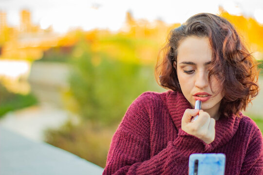Mujer joven de raza cauc&aacute;sica con el pelo corto pint&aacute;ndose los labios con un pintalabios rojos en un parque de Madrid 