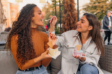 Two girls are having fun and eating delicious ice-cream in the cafe garden on a sunny day.