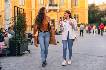 Fototapeta premium Two girls are strolling, talking and eating cone ice cream, and having much fun in the town.