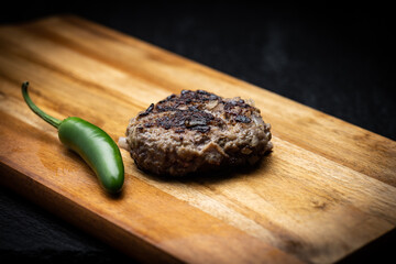Traditional Bulgarian ground meat patty called kufte on wooden surface next to green chili pepper
