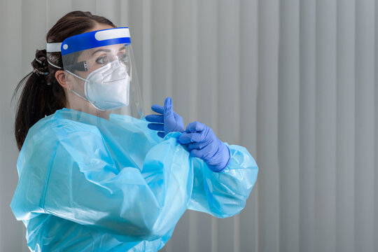 Nurse Is Putting On Her Protective Gloves While Wearing N95 Mask With Face Shield On Her Face 