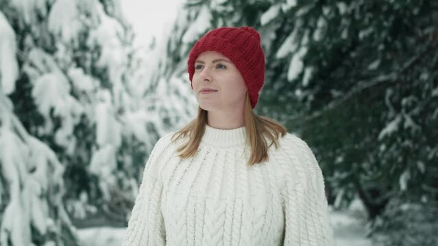 Caucasian woman wearing red hat walking in snowing forest. Shot with RED helium camera in 8K.