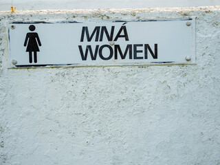 Sign women in Irish and English language on a changing room by a beach or toilet. Multi language culture concept. White wall with texture.