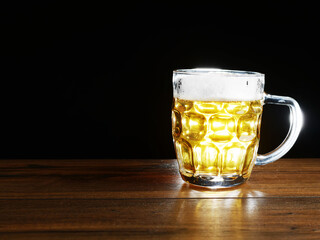 Full jar of lager beer with froth on a wooden table glowing in a dark. Alcohol consumption and sale. Copy space