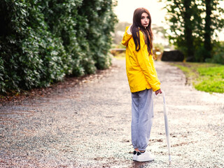 Teenager girl in yellow jacket holding translucent umbrella on a foot path in a forest park. Outdoor activity. Going out.