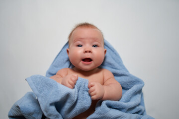 A smiling baby looks at the camera against a light-colored background with a blue towel