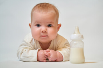 portrait of an infant in light clothing next to a bottle of milk on a light background