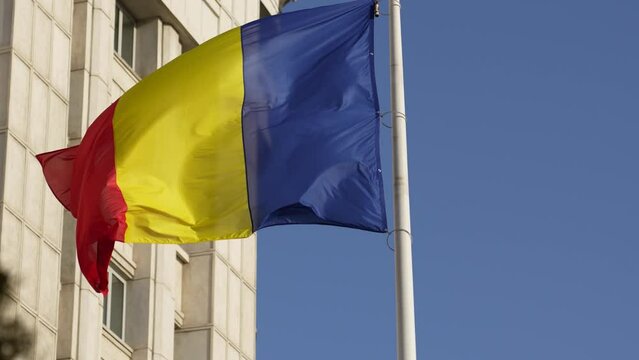 National flag of Romania. Romanian flag waving against blue sky clear background in slow motion.