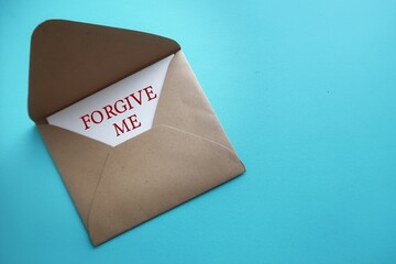 Card in craft envelope on blue copy space background with text written FORGIVE ME, to ask someone to forgive, to say sorry or apologize for mistake making