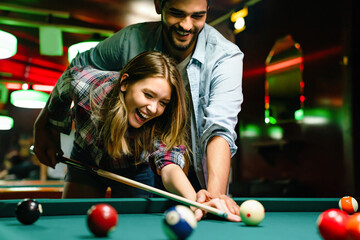 Happy young couple enjoying while playing billiard in bar. People entertainment fun concept