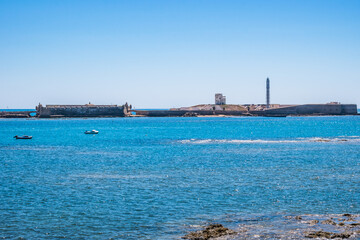 Rocks and boats in the turquoise sea and San Sebastian castle and fortress on the horizon, C&aacute;diz SPAIN
