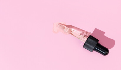 Flat lay of a pipette with pouring liquid serum on pink background. Copy space