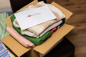 Fototapeta premium Clothes Donation. Box of warm cloth with donate label. Gathering items to be donated to charity