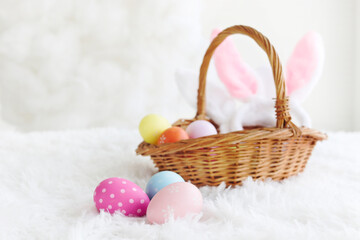 Fototapeta na wymiar Colorful Easter eggs on rug fluffy white fur carpetand with wicker basket and bunny rabbit ears headband, decoration and celebration spring beginning.