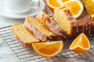 Fototapeta na wymiar Loaf of orange bread covered with a confectionery glaze with lemon juice and decorated with orange slices. Chiffon cake on a pastry grill next to cup of tea. White background