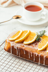 Loaf of orange bread covered with a confectionery glaze with lemon juice and decorated with orange slices. Chiffon cake on a pastry grill next to cup of tea. White background