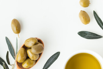 Wooden spoon full of green olives next to olive oil and leaves on the white background. Flat lay. Traditional Greek and Italian food ingredients