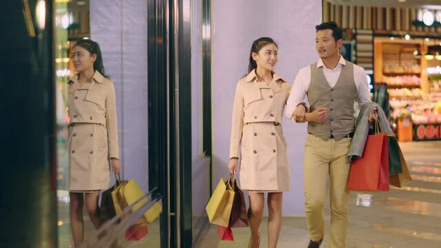 happy loving young asian couple walking in shopping mall with paper bags in hand