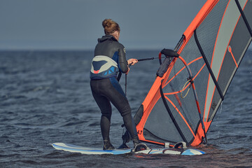 Mature woman windsurfer novice wants to raise the sail of a sailboard and continue surfing on a sunny autumn day.