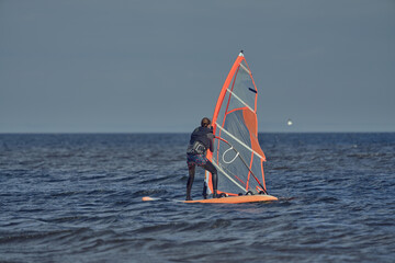 Mature woman windsurfer novice wants to raise the sail of a sailboard and continue surfing on a sunny autumn day.