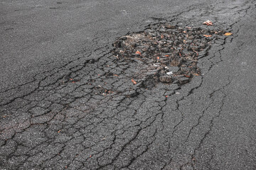 The paved road surface is damaged. Broken asphalt. Cracked tarmac street. Poor quality roadway is risk for driving.