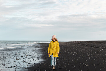 Blond Woman in Yellow Coat Walking on Beach with Black Sand, Diamond Beach in Iceland, Atlantic Ocean  