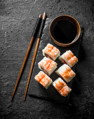 Fresh sushi rolls with shrimp on a stand with soy sauce and chopsticks.