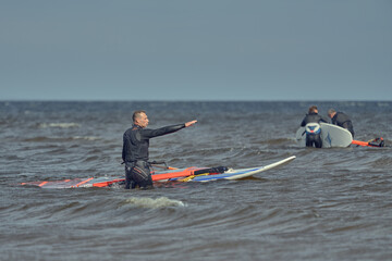 Windsurfers men and one woman stand in the water in shallow water on a sunny autumn day. They want to start surfing.