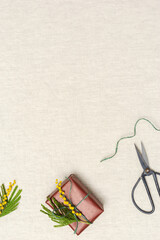 Gift boxes in red craft paper decorated natural mimosa flower on table beige tablecloth. Top view background with spring holiday present wrapping, cozy diy gifts, flat lay, copyspace