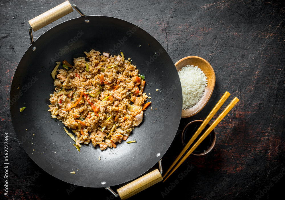 Sticker Chinese wok. Cooked rice in a wok pan and uncooked rice on a plate.