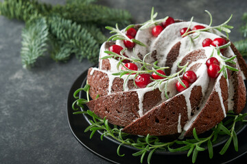 Christmas chocolate bundt cake. Traditional Christmas fruit cake with white glaze, cranberries and rosemary on dark backgroundChristmas decoration. Winter baking at Xmas or New Year. Copy space.