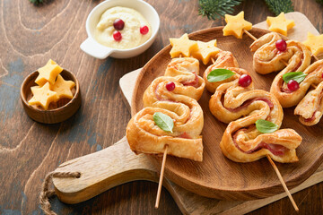 Christmas or New Year appetizer. Christmas tree shape puff pastry buns with cheese and ham. Group of Christmas tree shapes on wooden board. Festive idea for Christmas or New Year dinner. Top view.