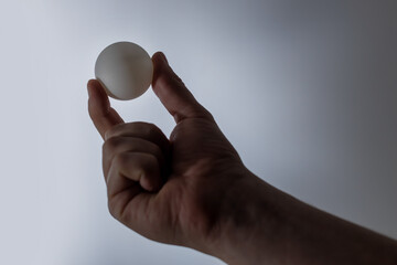 Man holds pingpong ball in a hand - grey background