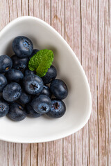 Raw blueberries in white bowl over wooden background. Sweet juicy wild berries for vitamin vegetarian dessert. Blueberry as vegan snack. Detox diet ingredient. Vertical frame.