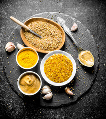 Different types of mustard on a stone Board with garlic.