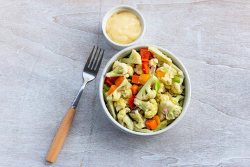 Healthy cauliflower salad in white bowl on wood background.