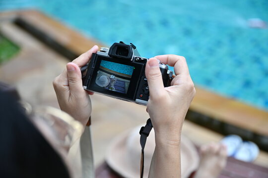 A female tourist raises a digital camera to take pictures while relaxing by the swimming pool. Woman holding the camera with both hands while taking pictures. photo of camera and blurry pool
