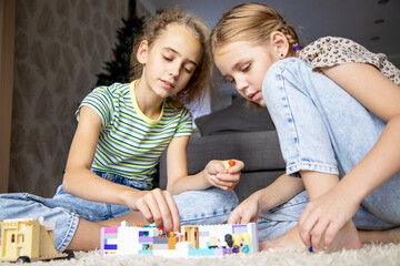 Two little sister girls play with multi-colored toy  blocks at home in the living room. Educational games for children. Mess in the game room.