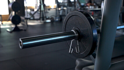 Close-up of chrome steel bar with black weight plate on the training apparatus in the gym. Body training and fitness for healthy lifestyle.