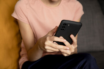 Teenage girl using smartphone, presses her finger, reads social networks on the Internet, types text or makes in-app purchases, mobile phone in two hands.