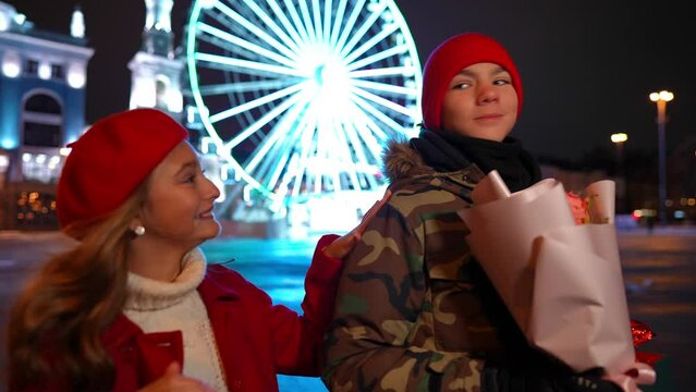 Loving confident teen boy looking away as girl surprising boyfriend tapping shoulder. Happy Caucasian couple dating on night city street on Valentine's. Slow motion