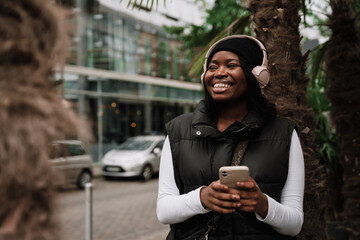 Fototapeta premium Smiling afro woman using mobile phone while standing outdoors at city street