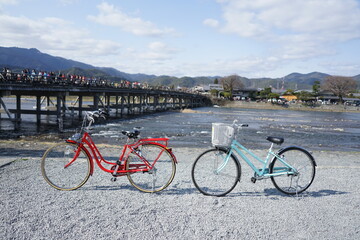 Fototapeta premium Red and light blue city bicycle parked beside the river with Kyoto Togetsu Bridge background