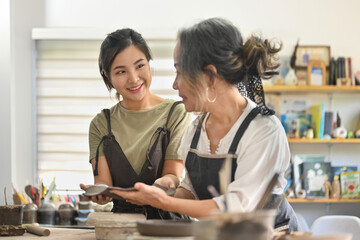 Fototapeta premium Earthenware workshop studio hobby or small business with Two diversity age of craftswomen shaping tableware from raw clay in workshop space.