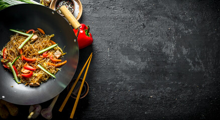 Cooked Chinese noodles cellophane wok with soy sauce in a bowl and with chopsticks.