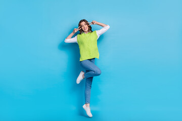 Full length portrait of carefree cheerful girl jumping hands fingers show v-sign near eyes isolated on blue color background