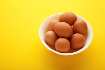 Top view of raw brown eggs on plate on yellow background. Eggs are a common ingredient in cooking.