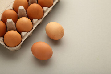 Chicken eggs in an open egg carton on grey. Top view with copy space. Natural healthy food and organic farming concept.