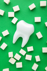 Fototapeta na wymiar Plastic tooth with sugar on green background. Caries and sugar concept. Dental care concept. Vertical photo